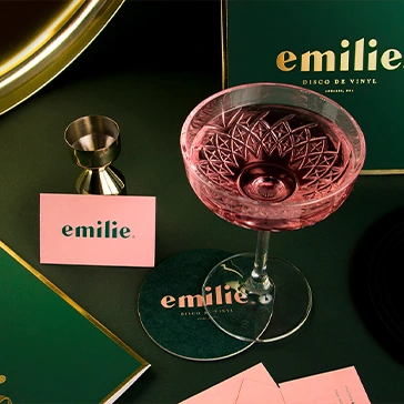 a glass of pink liquid next to a green and gold plate